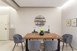 A dining area with a wooden table, four grey chairs, a black circular shelf, two candles, and a vase with flowers.