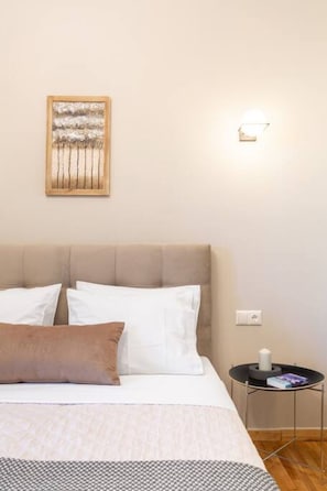 A bedroom with a bed, pillows, a nightstand, a wall-mounted lamp, and a framed picture.