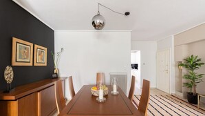 A dining area with a wooden table, chairs, a pendant light, framed pictures on the wall, and a potted plant. - Comfortable & Quiet Family APT Near Acropolis (Athina)