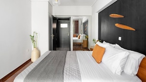 A modern hotel room with a large bed, a dark accent wall, and a view into the adjacent room. - Comfortable & Quiet Family APT Near Acropolis (Athina)