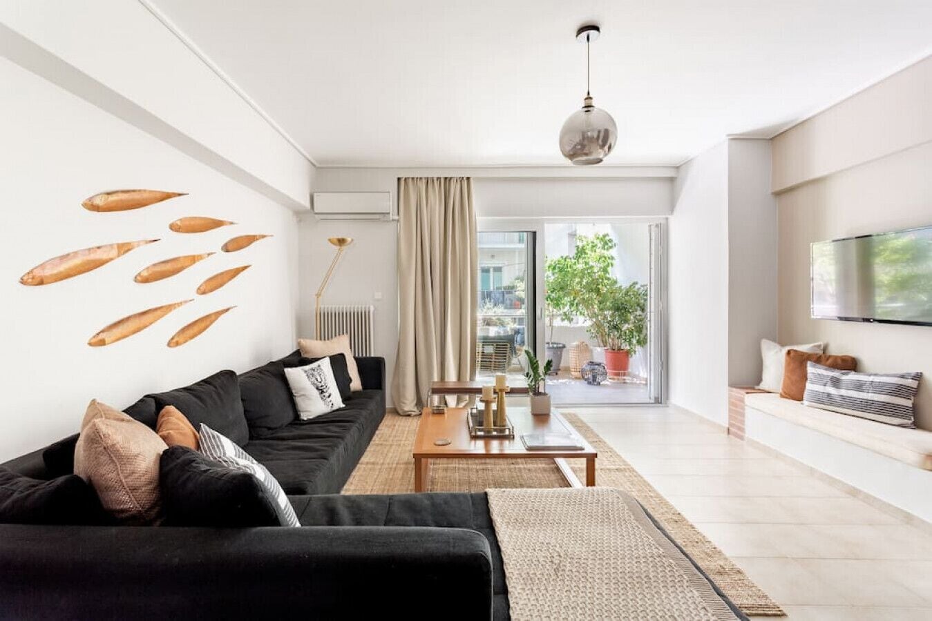 A modern living room with a black sofa, a wooden coffee table, and a large window with a view of the outdoors.
