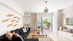 A modern living room with a black sofa, a wooden coffee table, and a large window with a view of the outdoors. - Comfortable & Quiet Family APT Near Acropolis (Athina)
