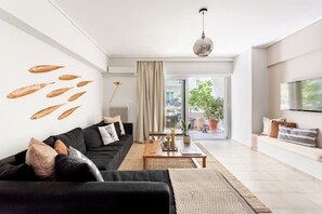 A modern living room with a black sofa, a wooden coffee table, and a large window with a view of the outdoors. - Comfortable & Quiet Family APT Near Acropolis (Athina)