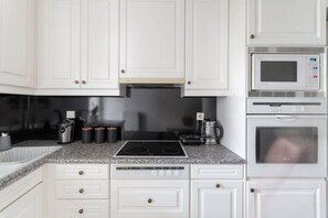 A kitchen with white cabinets, a black induction cooktop, a coffee maker, and a microwave. - Comfortable & Quiet Family APT Near Acropolis (Athina)