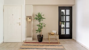 A hallway with a potted plant, a small table with a bowl, and a black door. - Comfortable & Quiet Family APT Near Acropolis (Athina)