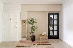 A hallway with a potted plant, a small table with a bowl, and a black door. - Comfortable & Quiet Family APT Near Acropolis (Athina)