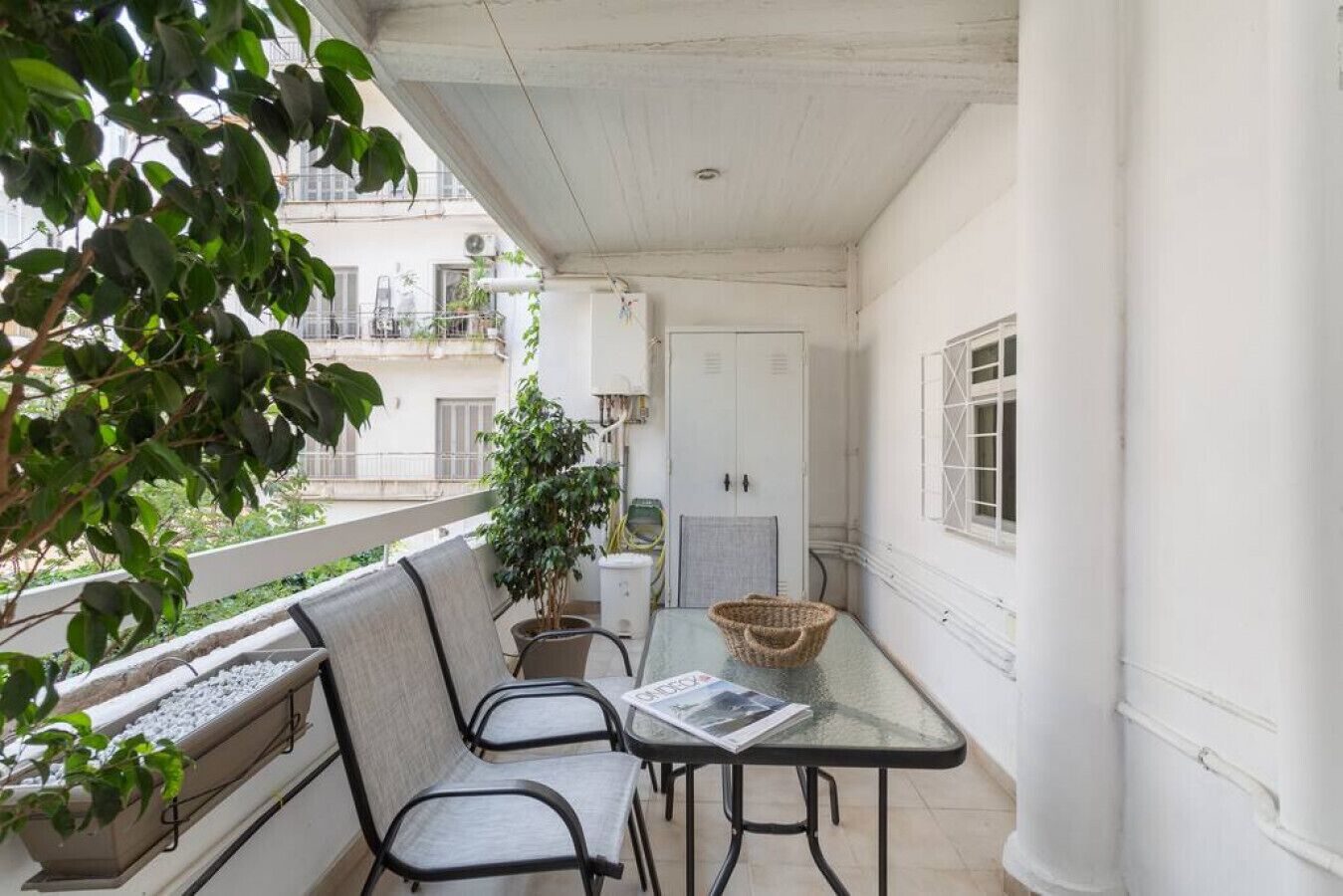 A balcony with a table and chairs, a potted plant, and a view of the building across the street.