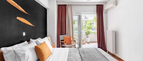A modern hotel room with a large bed, a black accent wall, a view of the outdoors, and a chair by the window.