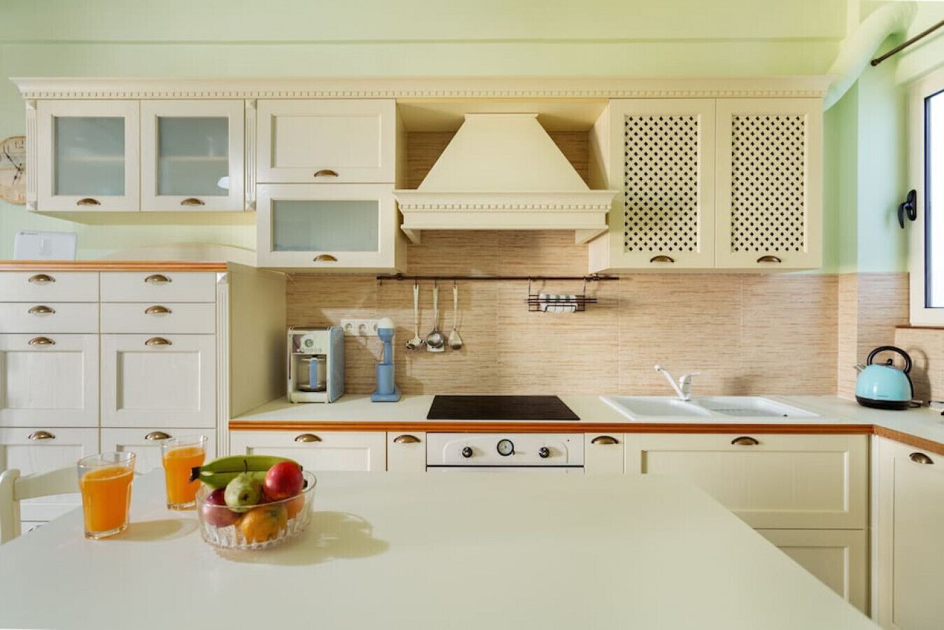A kitchen with white cabinets, a stove, a sink, and a fruit bowl on the counter.