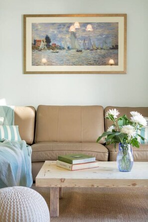 Ein Wohnzimmer mit einem beigefarbenen Sofa, einem Couchtisch mit Büchern und einer Blumenvase sowie einem Gemälde über dem Sofa.