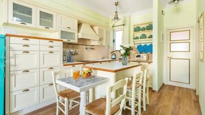 A kitchen with white cabinets, a wooden countertop, and a dining area with white chairs. - Bright, Calming Retreat With Balcony Near Metro! (Menemeni)