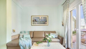 A living room with a beige sofa, a coffee table, and a painting on the wall. - Bright, Calming Retreat With Balcony Near Metro! (Menemeni)