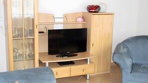 A living room with a television on a wooden stand, a blue sofa, and a cabinet with glass doors. - Apartment 1 with Terrace, Garden and Wi-Fi (Überlingen)