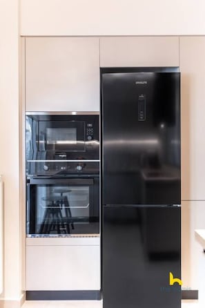 A modern kitchen with a built-in oven and a black refrigerator. - Minimal 2-BDR Apt Near Acropolis By The Homis (Athina)