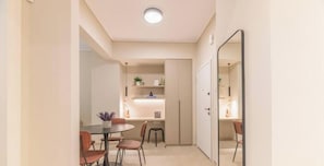 A modern interior with a dining area, kitchenette, and a mirror reflecting the space. - Minimal 2-BDR Apt Near Acropolis By The Homis (Athina)