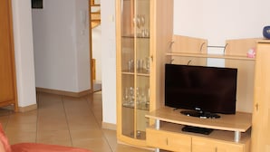 A living room with a flat-screen TV on a wooden stand, a glass cabinet with wine glasses, and a red sofa. - Apartment '2' with Balcony, Garden and Wi-Fi (Überlingen)