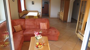 A living room with a sofa, a dining table, and a kitchen area in the background. - Apartment '2' with Balcony, Garden and Wi-Fi (Überlingen)