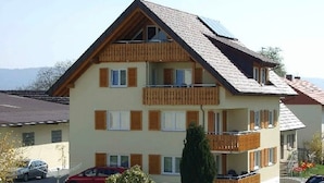 A multi-story residential building with a sloped roof, wooden balconies, and a car parked in the driveway. - Apartment '2' with Balcony, Garden and Wi-Fi (Überlingen)