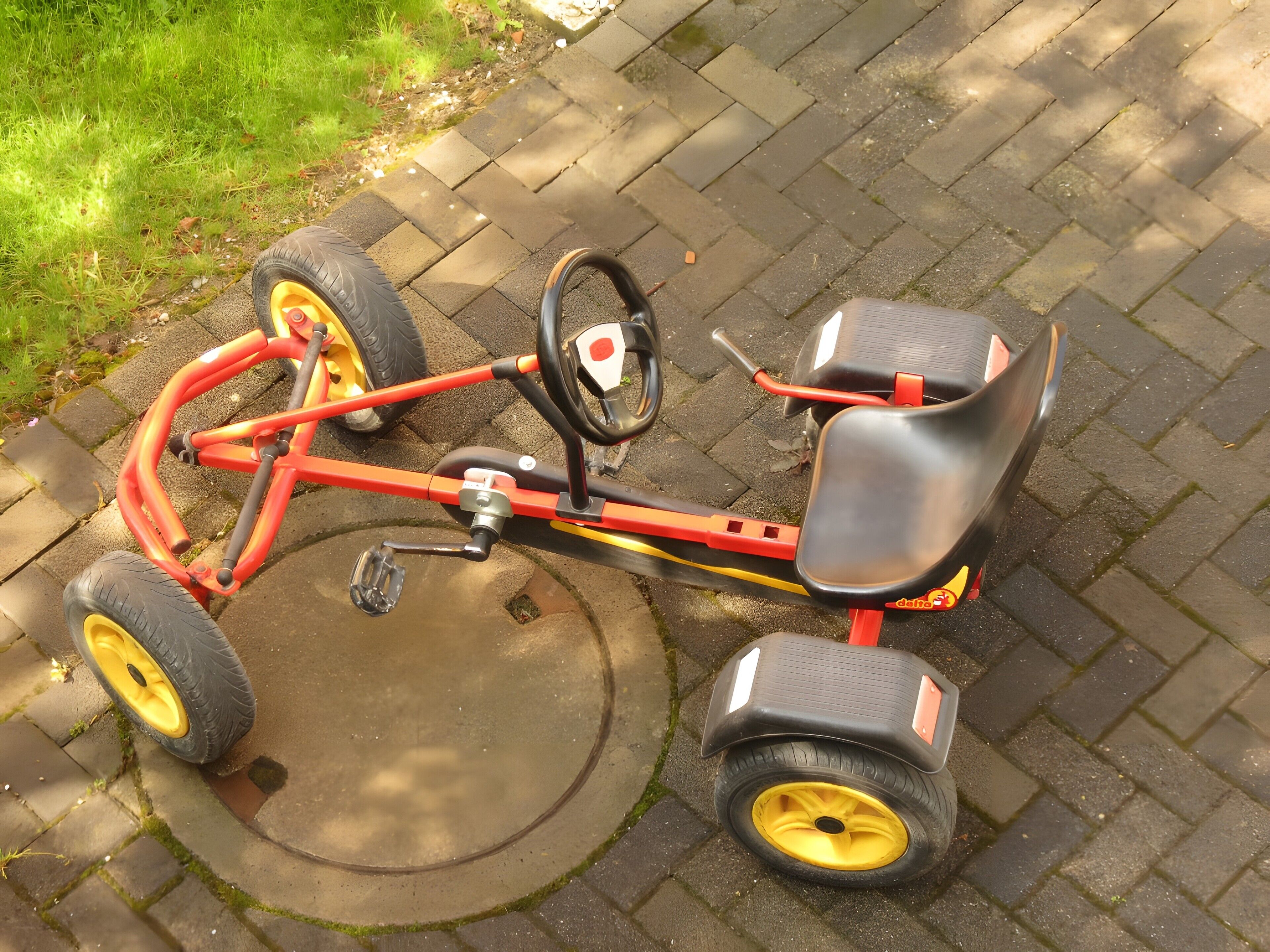 A red tricycle with yellow wheels parked on a paved surface.