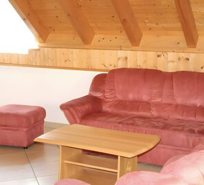 A wooden ceiling with visible beams, a red sofa, a matching ottoman, and a wooden table.