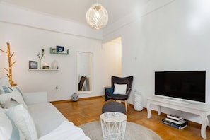 A modern living room with a sofa, a chair, a TV on a stand, and a decorative light fixture. - Head for Acropolis from a Romantic Nest in Koukaki (Athina)