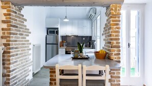 A kitchen with white cabinets, a central island with chairs, a microwave, and a refrigerator. - Head for Acropolis from a Romantic Nest in Koukaki (Athina)