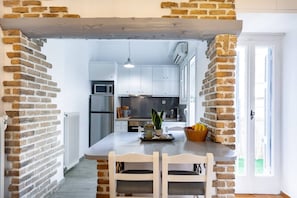 A kitchen with white cabinets, a central island with chairs, a microwave, and a refrigerator. - Head for Acropolis from a Romantic Nest in Koukaki (Athina)