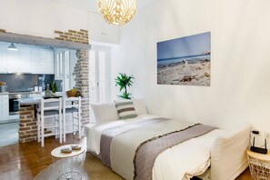 A compact room with a kitchenette, a bed, a dining area, and a beach-themed wall art. - Head for Acropolis from a Romantic Nest in Koukaki (Athina)