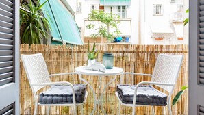 A balcony with two white wicker chairs, a round table, and a bamboo fence. - Head for Acropolis from a Romantic Nest in Koukaki (Athina)
