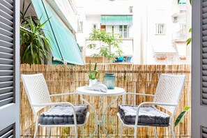 A balcony with two white wicker chairs, a round table, and a bamboo fence. - Head for Acropolis from a Romantic Nest in Koukaki (Athina)