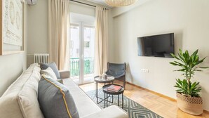 Een moderne woonkamer met een bank, een klein rond tafeltje, een stoel, een televisie en een potplant.