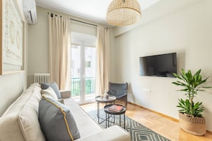A modern living room with a sofa, a small round table, a chair, a television, and a potted plant. - Discover Athens from Urban Hideaway,Acropolis View (Athina)
