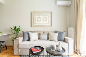 A living room with a sofa, two side tables, a framed artwork, a radiator, and a potted plant. - Discover Athens from Urban Hideaway,Acropolis View (Athina)