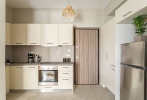 A modern kitchen with light-colored cabinets, a built-in oven, a stainless steel refrigerator, and a wooden door. - Discover Athens from Urban Hideaway,Acropolis View (Athina)