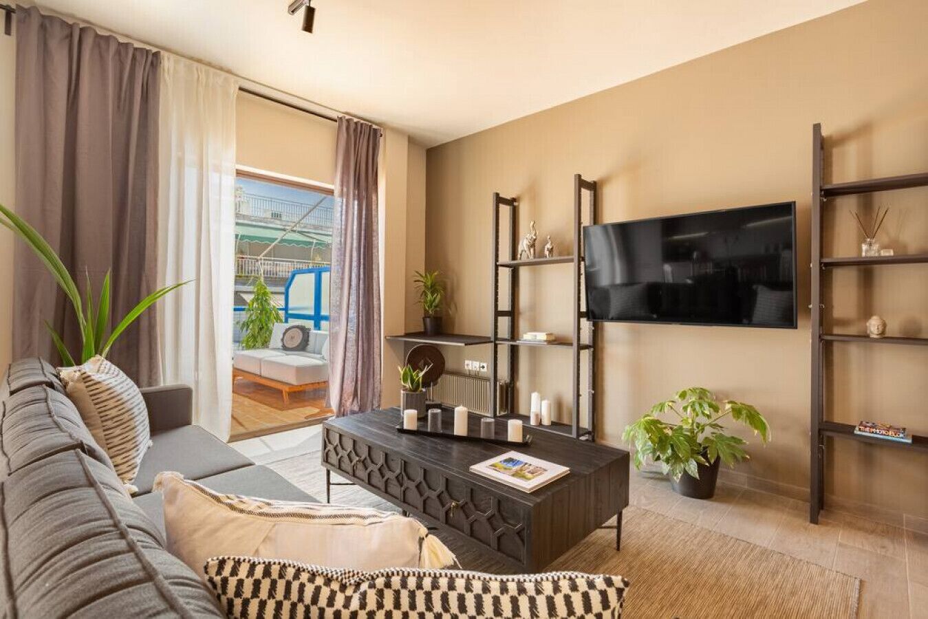 A modern living room with a sofa, coffee table, and TV. There is a balcony with a view.