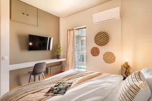 Quarto de hotel com cama, escrivaninha com cadeira, televisão e janela com cortinas.