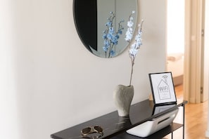 Un intérieur moderne agrémenté d’un miroir rond, d’un vase avec des fleurs bleues, d’un panneau encadré indiquant le réseau Wi-Fi et d’une imprimante posée sur une console noire.