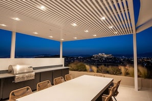 An outdoor patio with a grill, dining table, and chairs, overlooking a cityscape and a hill with a castle-like structure. - Kalypso, Urban APT w/ Unique Views of Acropolis! (Athina)