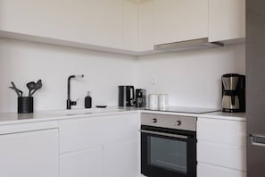 Une cuisine moderne avec des meubles blancs, une cuisinière noire, une machine à café et une bouilloire.