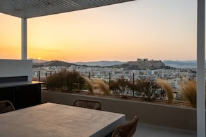Une terrasse avec une table et des chaises, d’où l’on peut admirer un panorama urbain avec une colline imposante et une structure qui ressemble à un château.