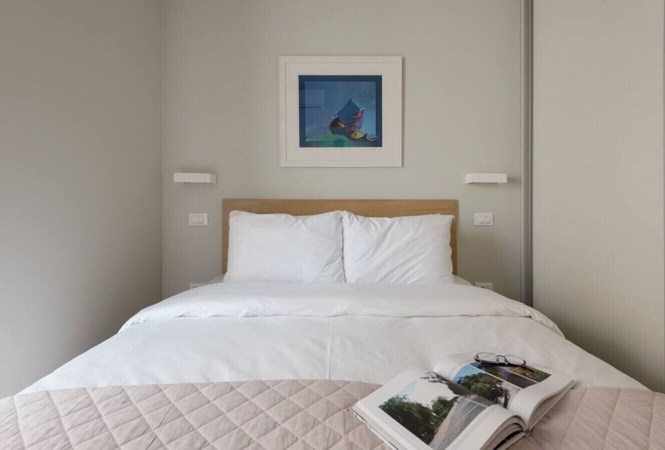 A neatly made bed with white linens, a quilted blanket, and a magazine on the side.