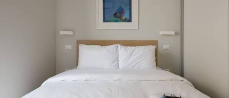 A neatly made bed with white linens, a quilted blanket, and a magazine on the side.