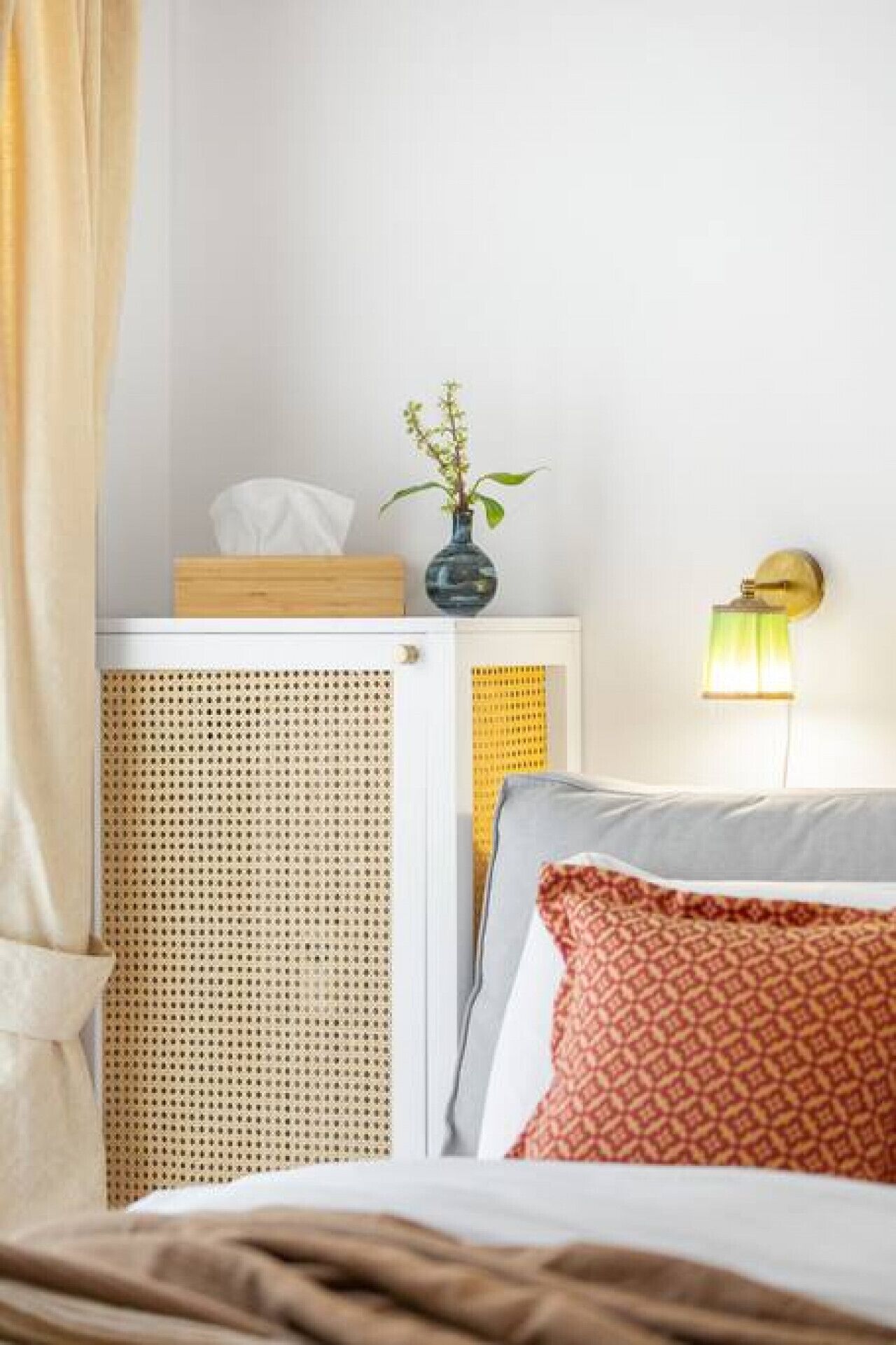 A neatly arranged hotel room with a bed, a bedside table with a vase of flowers, a lamp, and a window with curtains.