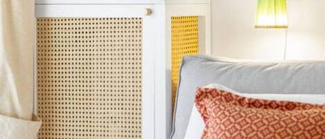 A neatly arranged hotel room with a bed, a bedside table with a vase of flowers, a lamp, and a window with curtains.