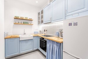 A compact kitchen with light blue cabinets, a wooden countertop, a sink, a stove, and a refrigerator. - Chill Out In Retropolitan Hideaway at Alsos Park (Athina)