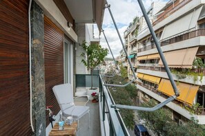 A balcony with a white chair, a small table with a bottle and a mug, and a potted plant. - Chill Out In Retropolitan Hideaway at Alsos Park (Athina)