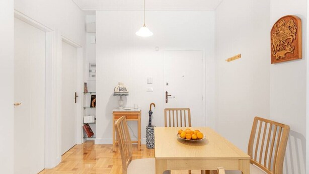 A dining area with a wooden table, four chairs, a bowl of fruit, a lamp, and a decorative wooden carving on the wall. - Chill Out In Retropolitan Hideaway at Alsos Park (Athina)