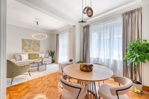 Ein modernes Wohnzimmer mit einem runden Esstisch, einer Couch und einem großen Fenster mit Vorhängen.