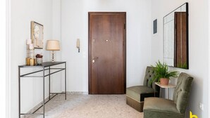 A hallway with a wooden door, a console table with a lamp, a chair, and a potted plant. - Contemporary 2-BDR APT near Kalimarmaro & Alsos! (Athina)