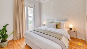 A bedroom with a large bed, a potted plant, a bedside table with a lamp, and a view of the outdoors through a sliding door. - Contemporary 2-BDR APT near Kalimarmaro & Alsos! (Athina)